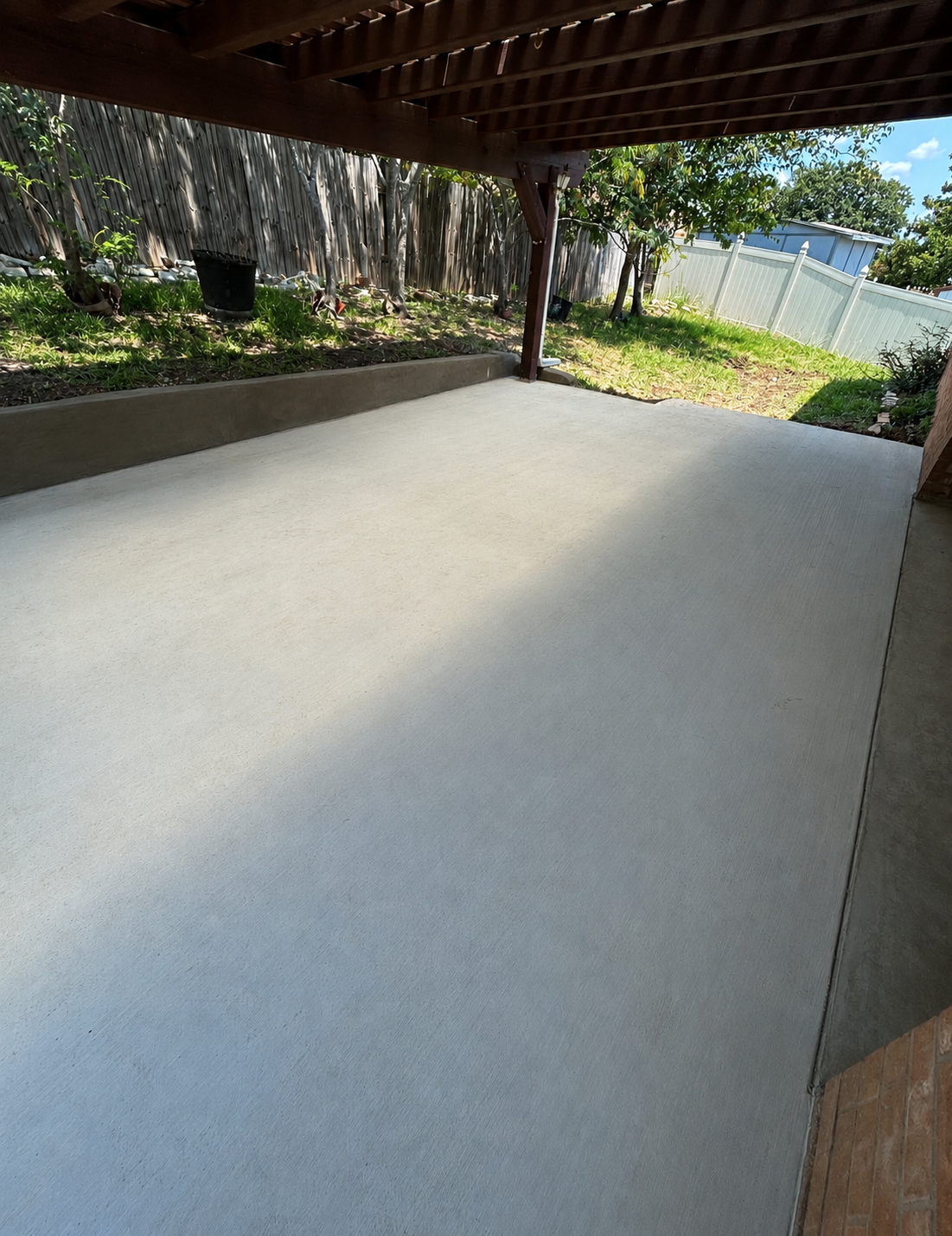 Finished concrete patio under wooden pergola with retaining wall by Martinez Construction