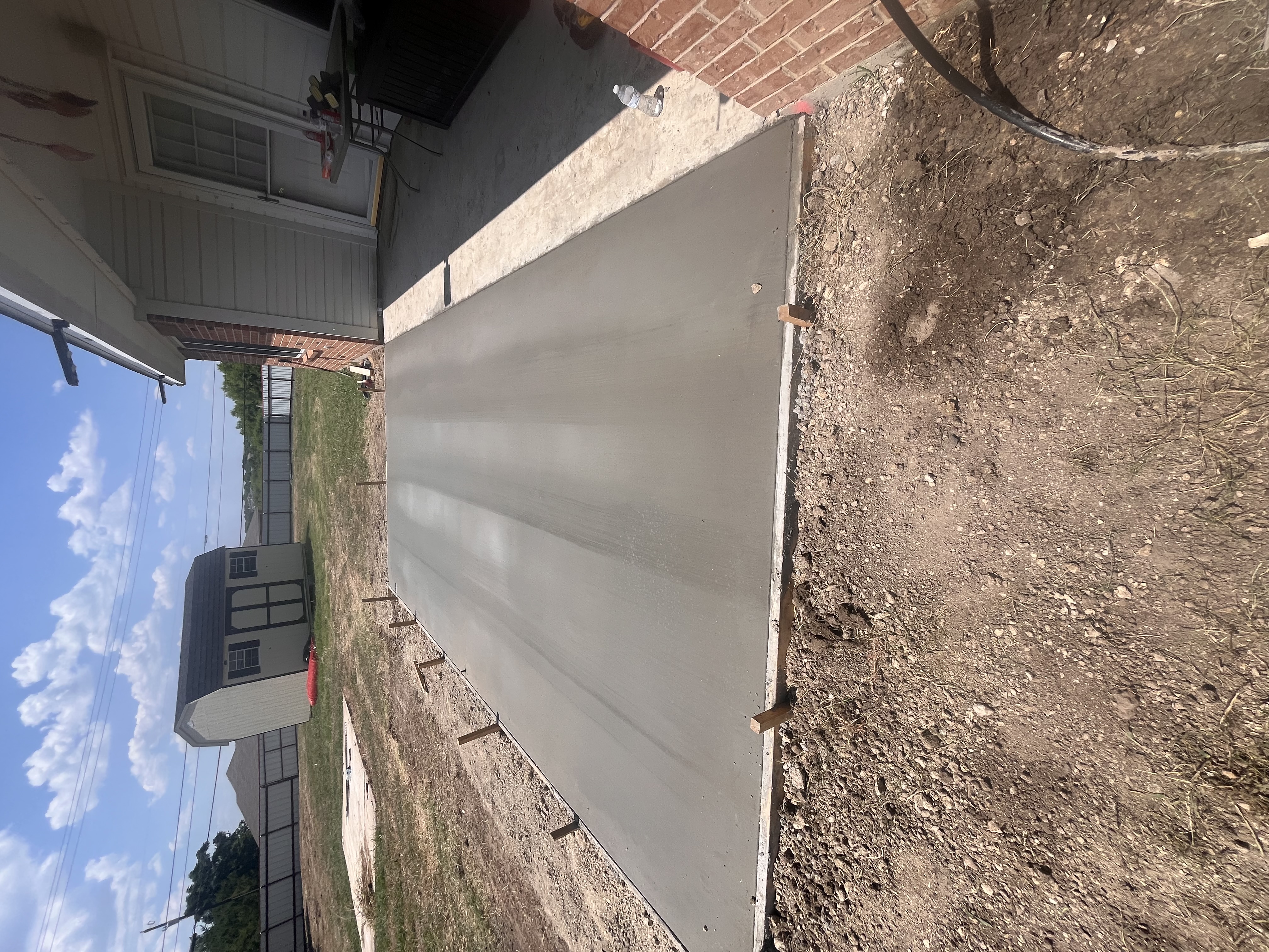 Freshly poured and smoothed concrete porch slab with wooden formwork curing in front of a red brick house under a blue sky in Killeen TX by Martinez Construction