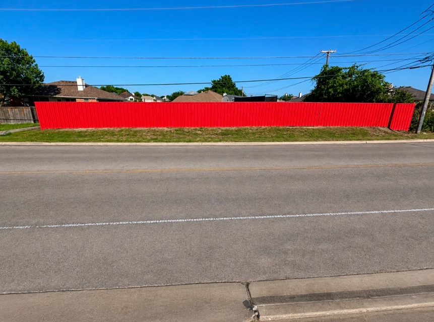 Long bright red vertical-slat fence along a suburban street with blue sky and power lines upper right by Martinez Construction fencing contractor