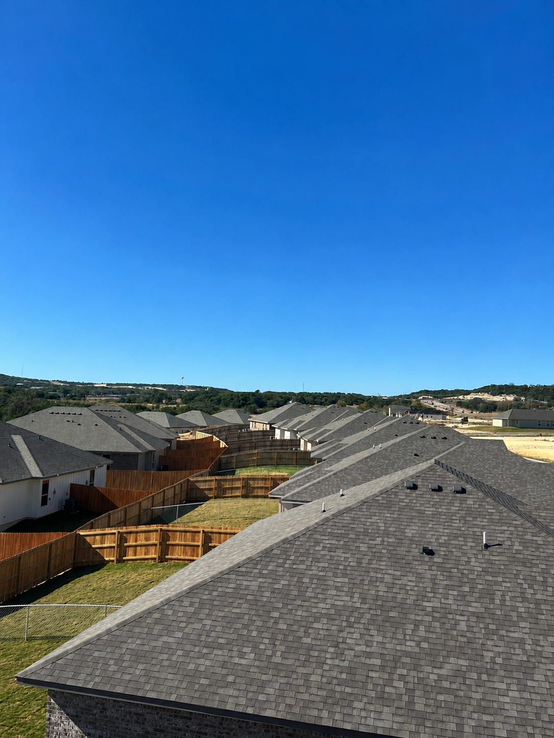 Aerial drone view of gray shingle roofs, wood fences, blue sky, and rolling green hills — Martinez Construction roofing contractor Bell County TX
