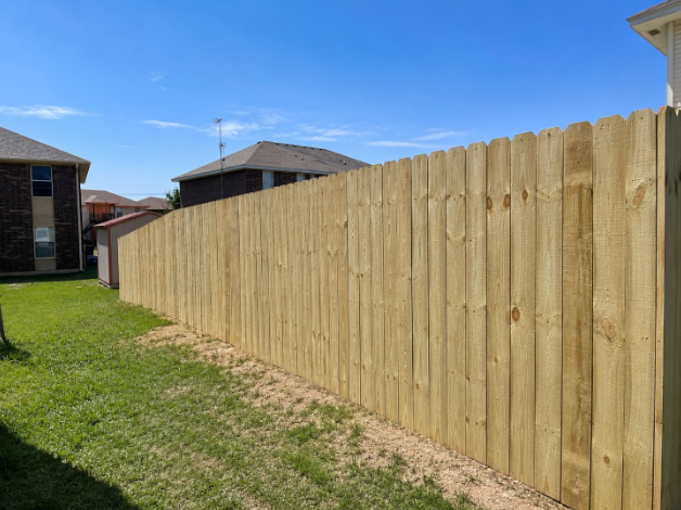 Clean light-tan wood privacy fence with vertical slats and dog-ear tops along a suburban lawn in Temple TX by Martinez Construction